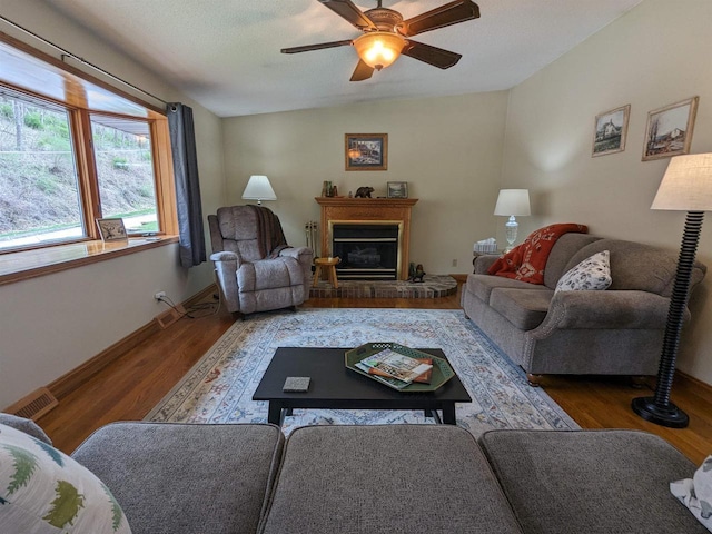 living area featuring a glass covered fireplace, wood finished floors, visible vents, and baseboards