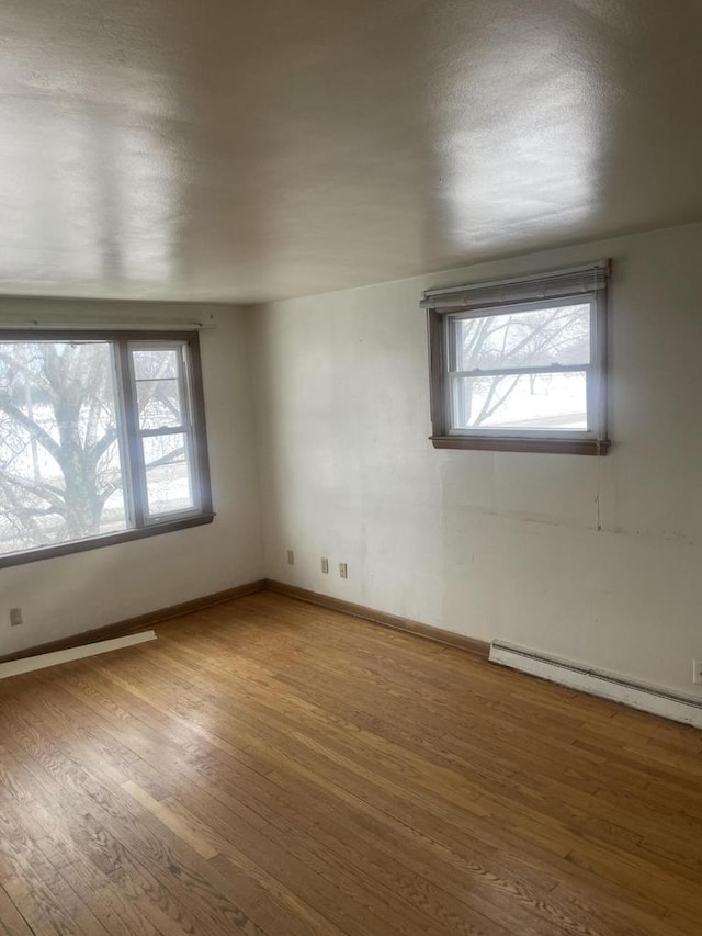 empty room with baseboards, a baseboard radiator, wood finished floors, and a healthy amount of sunlight