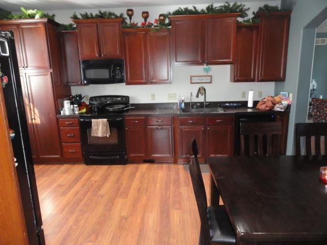 N5194 Blue Valley Rd, Hartford, WI 53027 - kitchen featuring black appliances, a sink, dark brown cabinets, dark countertops, and light wood-style floors