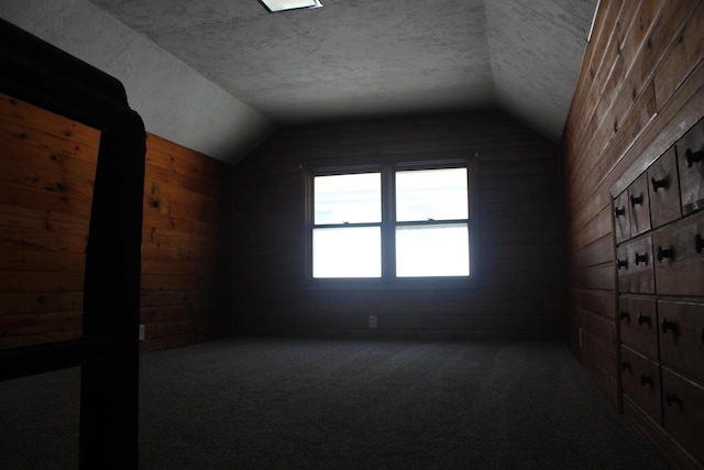 additional living space with carpet floors, wood walls, vaulted ceiling, and a textured ceiling