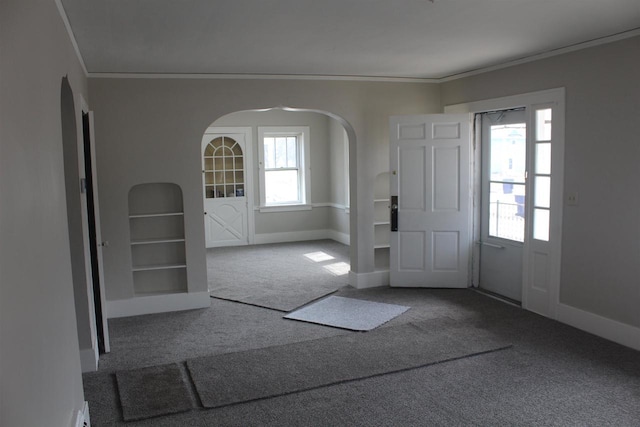 carpeted entryway with arched walkways, crown molding, and baseboards