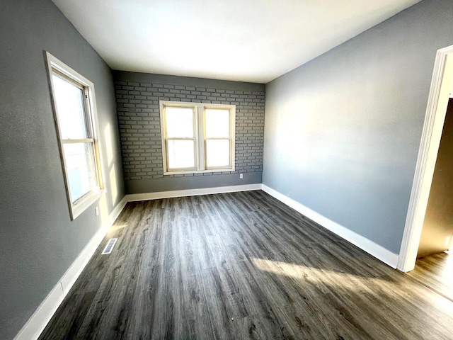 empty room with a healthy amount of sunlight, dark wood-style floors, baseboards, and visible vents