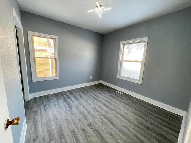 spare room featuring a wealth of natural light, visible vents, baseboards, and wood finished floors