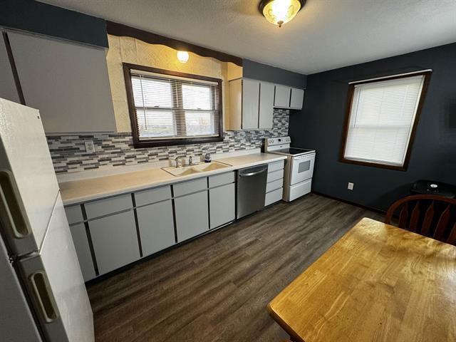 kitchen with a sink, light countertops, stainless steel dishwasher, white range with electric stovetop, and dark wood finished floors