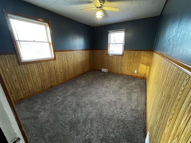 unfurnished room featuring a wainscoted wall, ceiling fan, wood walls, and visible vents