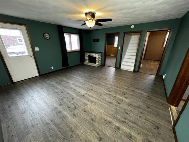 unfurnished living room with dark wood finished floors, a fireplace, and ceiling fan