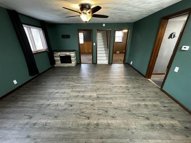 unfurnished living room with ceiling fan, a fireplace, wood finished floors, and baseboards