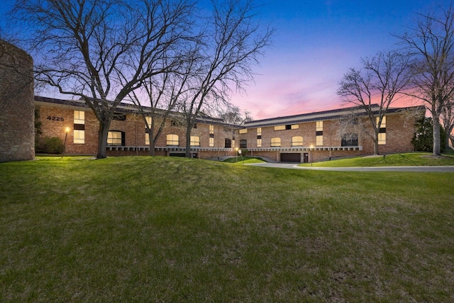 back of property at dusk featuring a lawn and brick siding