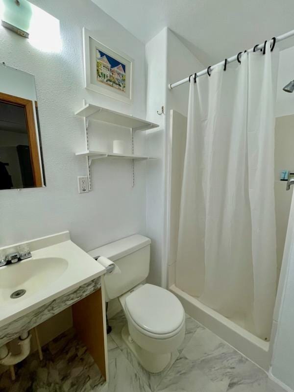 bathroom with marble finish floor, a stall shower, a sink, and toilet