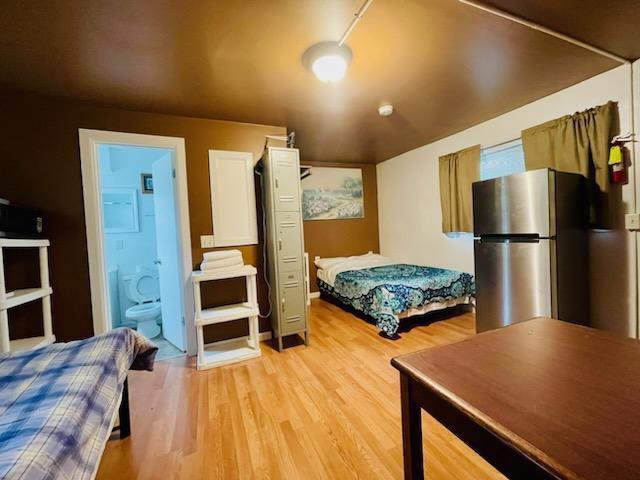 bedroom featuring light wood-style flooring, ensuite bathroom, and freestanding refrigerator