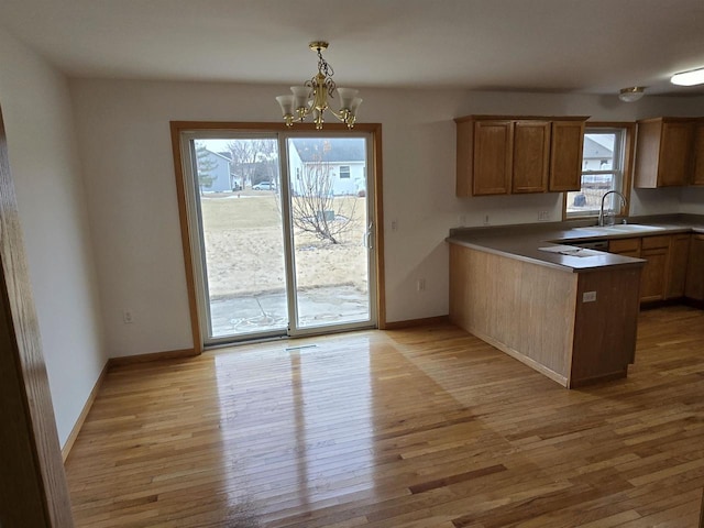 kitchen with hanging light fixtures, light wood-style flooring, a sink, plenty of natural light, and a peninsula