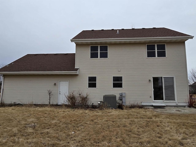 back of house with a shingled roof, cooling unit, and a lawn