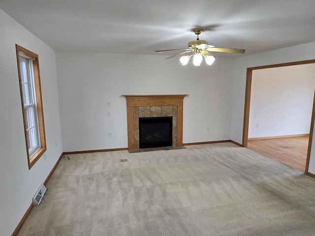 unfurnished living room with visible vents, a tiled fireplace, light carpet, ceiling fan, and baseboards