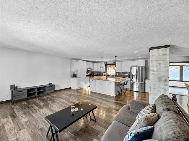 living room featuring ornate columns, recessed lighting, wood finished floors, and baseboards