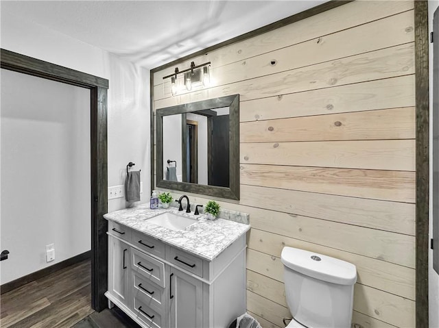 bathroom featuring toilet, wood finished floors, vanity, and wooden walls