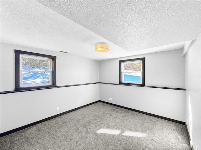 spare room with light colored carpet, visible vents, baseboards, and a textured ceiling