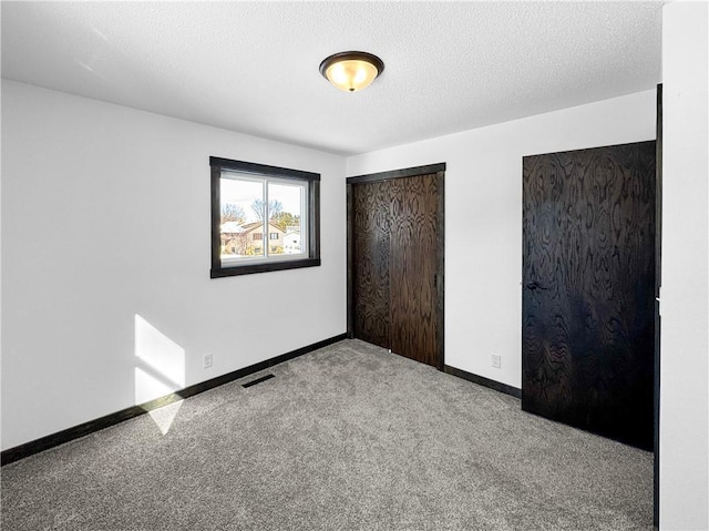 unfurnished bedroom with multiple closets, visible vents, light colored carpet, a textured ceiling, and baseboards