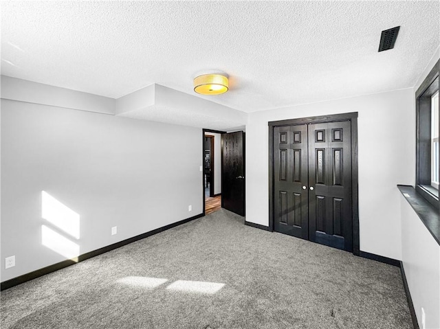 unfurnished bedroom with carpet floors, a closet, visible vents, a textured ceiling, and baseboards