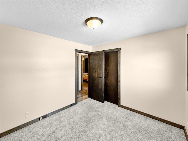 spare room with a textured ceiling, light colored carpet, and baseboards