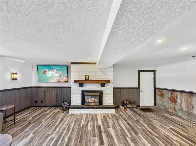 unfurnished living room with a wainscoted wall, a fireplace, wooden walls, a textured ceiling, and wood finished floors