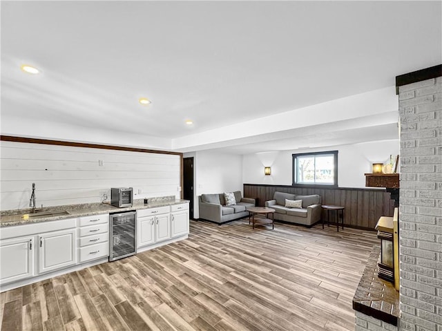 interior space featuring beverage cooler, a sink, white cabinetry, open floor plan, and light wood-type flooring