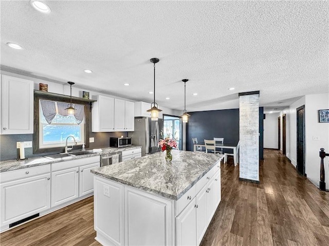 kitchen featuring pendant lighting, stainless steel appliances, white cabinets, a kitchen island, and a sink