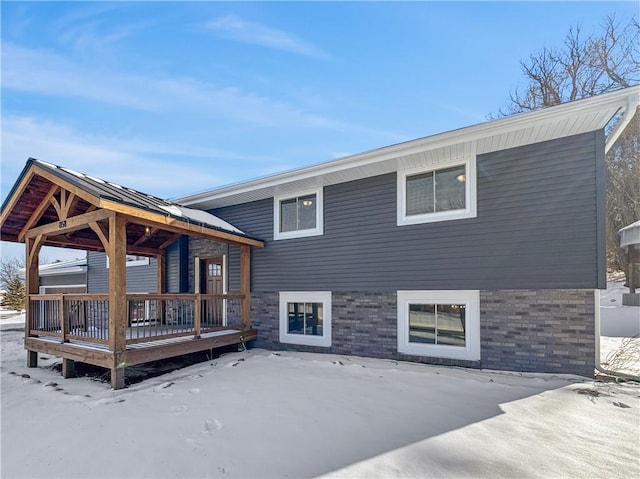 snow covered property featuring a wooden deck and brick siding