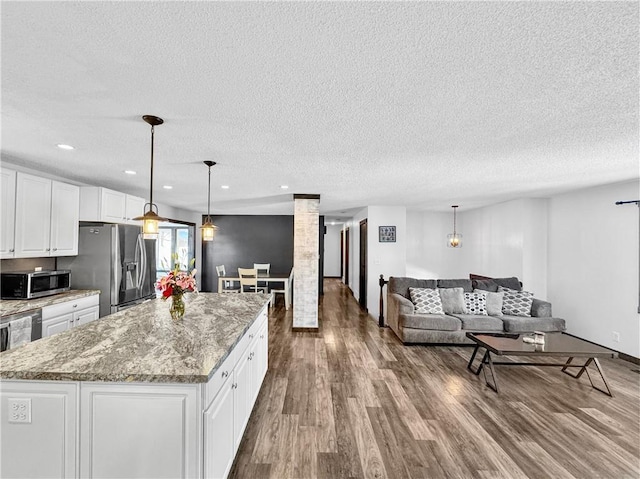 kitchen with stainless steel appliances, hanging light fixtures, open floor plan, white cabinets, and a kitchen island