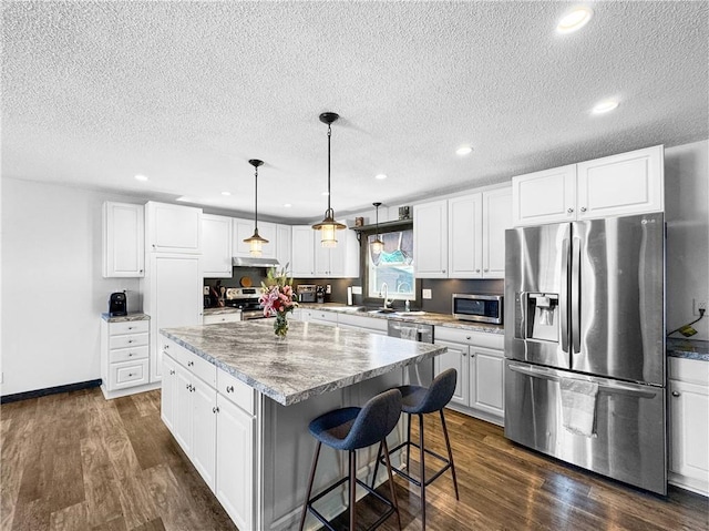 kitchen featuring white cabinets, decorative light fixtures, a center island, stainless steel appliances, and under cabinet range hood