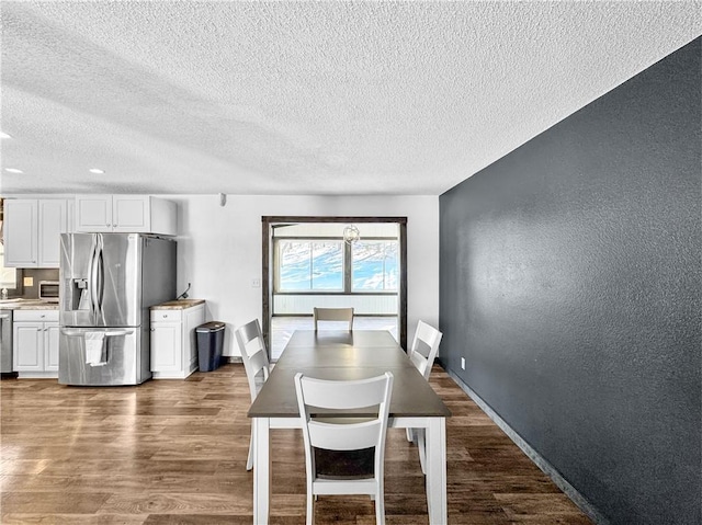 dining room featuring dark wood-style floors, a textured wall, a textured ceiling, and baseboards