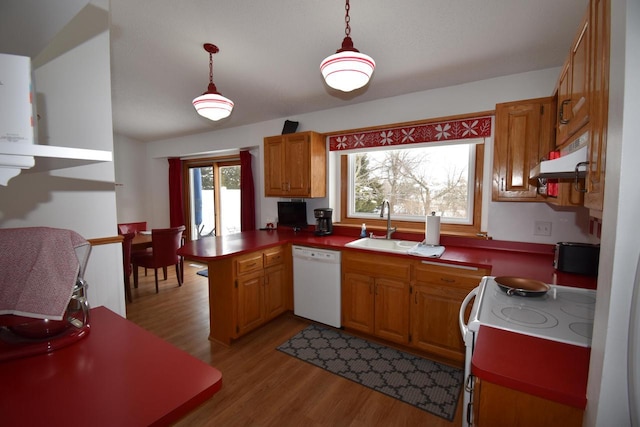 kitchen with white appliances, brown cabinetry, a peninsula, pendant lighting, and a sink