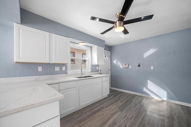 kitchen with a textured wall, dark wood-type flooring, a sink, and white cabinets