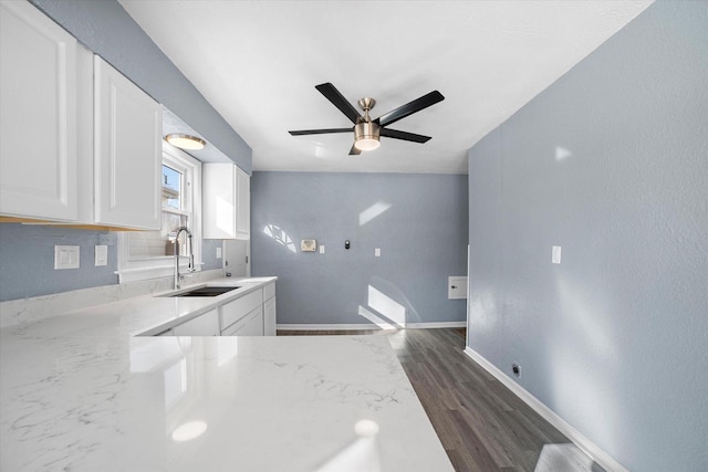 kitchen featuring dark wood-type flooring, white cabinetry, a sink, light stone countertops, and baseboards