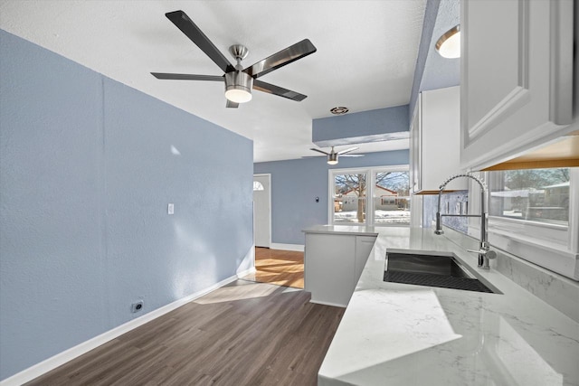 kitchen featuring baseboards, a ceiling fan, dark wood-style flooring, white cabinetry, and a sink