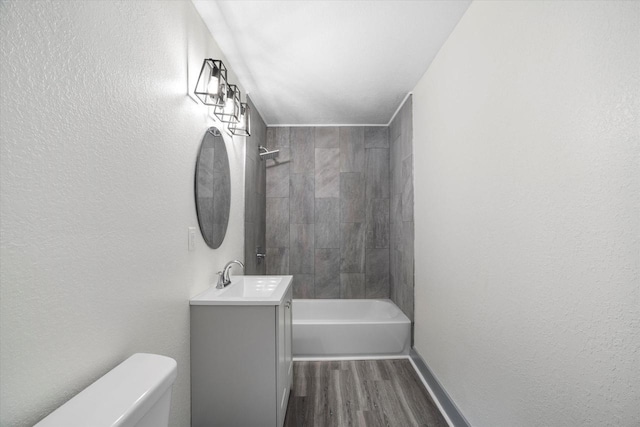 bathroom featuring a textured wall, toilet, wood finished floors, vanity, and  shower combination