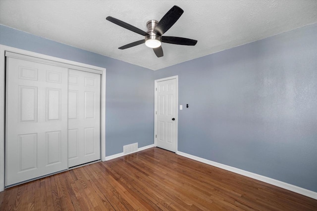 unfurnished bedroom with a closet, visible vents, a textured ceiling, wood finished floors, and baseboards