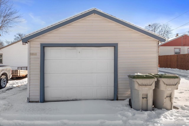 snow covered garage with a garage and fence