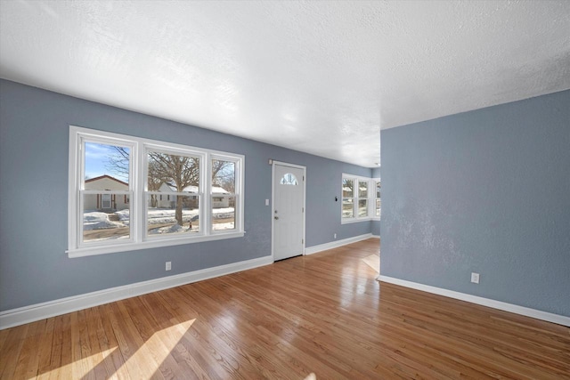 unfurnished living room with a textured ceiling, wood finished floors, and baseboards