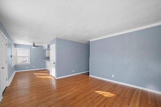 interior space featuring a ceiling fan, ornamental molding, baseboards, and wood finished floors