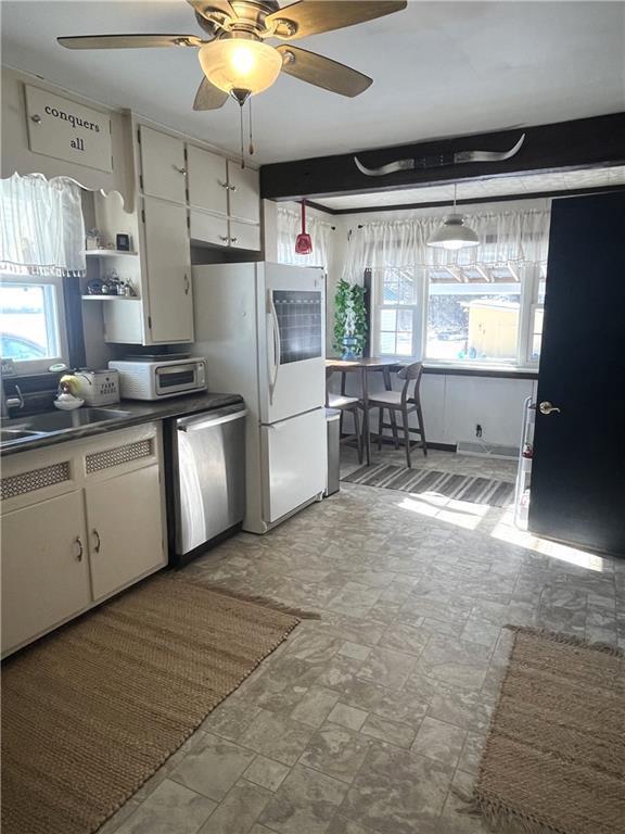 kitchen featuring a wealth of natural light, dark countertops, white cabinetry, and stainless steel dishwasher