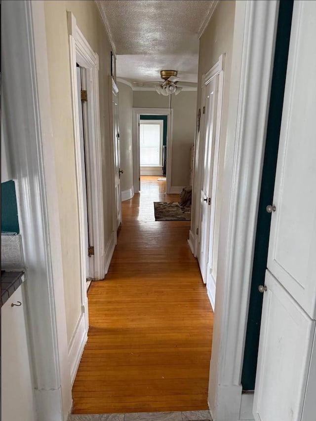 corridor featuring light wood-type flooring, baseboards, and a textured ceiling