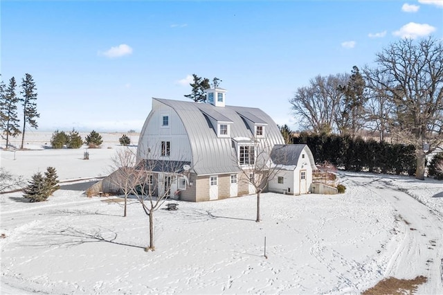 snow covered property featuring a garage, an outdoor structure, a barn, and a gambrel roof