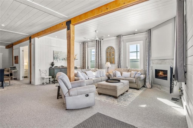 living room with a ceiling fan, wooden ceiling, beamed ceiling, a lit fireplace, and carpet flooring