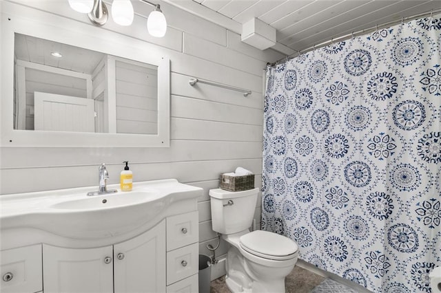 bathroom with toilet, curtained shower, wooden walls, and vanity