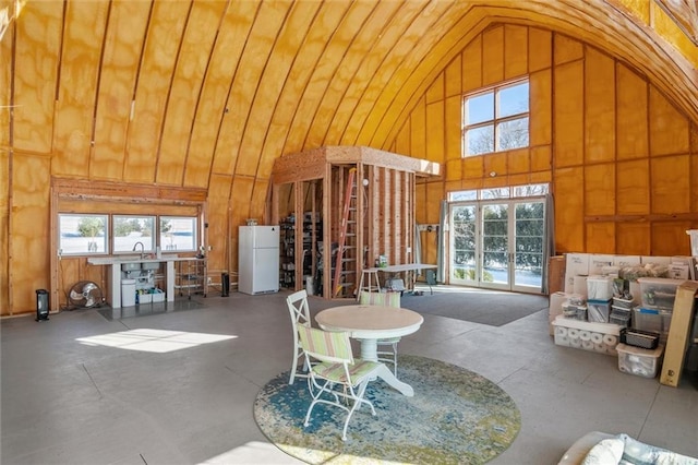 miscellaneous room featuring high vaulted ceiling, concrete floors, and wooden walls