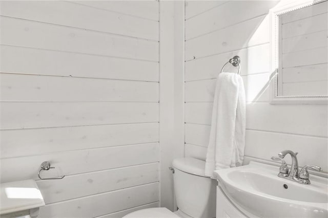 half bath with toilet, wooden walls, and vanity