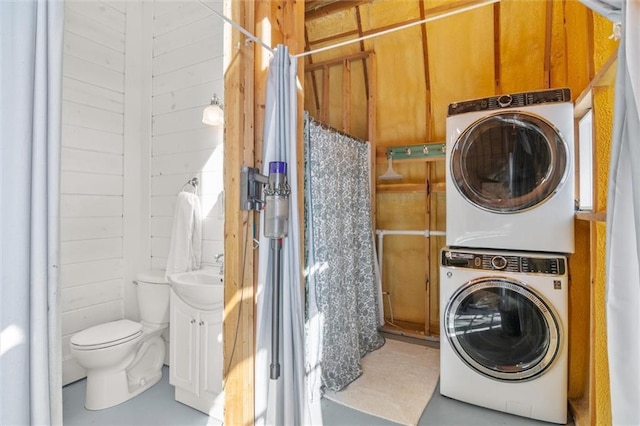 clothes washing area with a sink, laundry area, wooden walls, and stacked washer / dryer