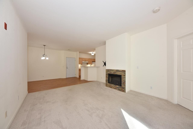 unfurnished living room featuring a notable chandelier, a stone fireplace, baseboards, and light colored carpet