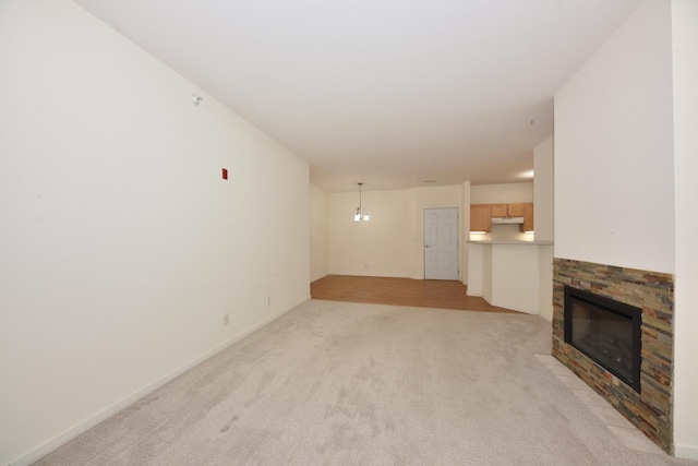 unfurnished living room with light carpet, baseboards, and a stone fireplace