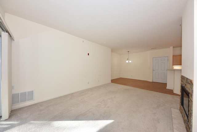 unfurnished living room featuring light carpet, a fireplace, visible vents, and a notable chandelier